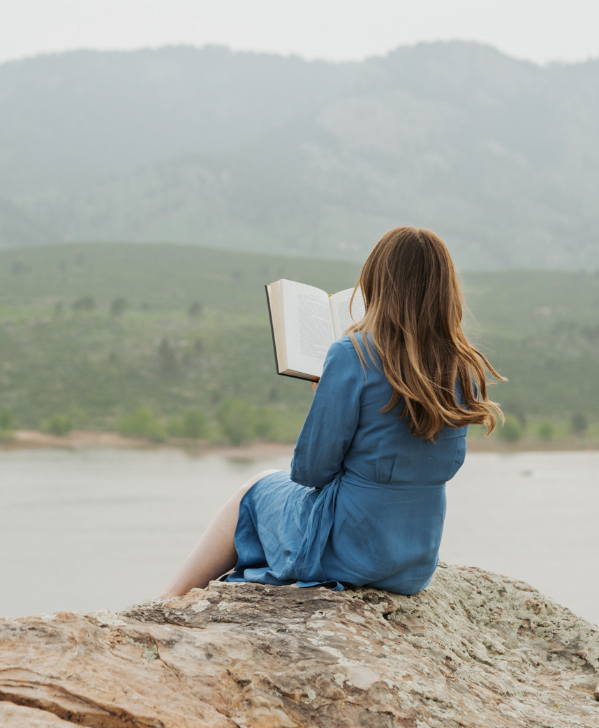Woman sits on cliff reading a book. Sirène Storyhouse provides book editing services.
