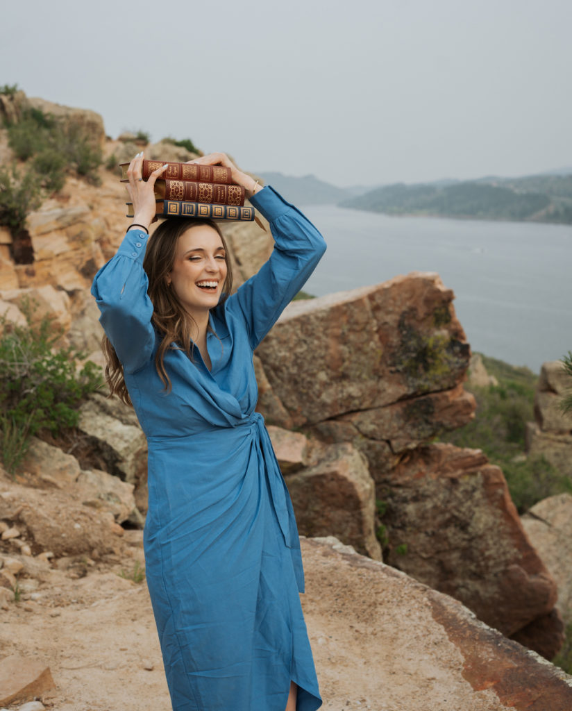 Woman wearing a blue dress holds books on her head. Learn about professional book editor Lily Capstick.